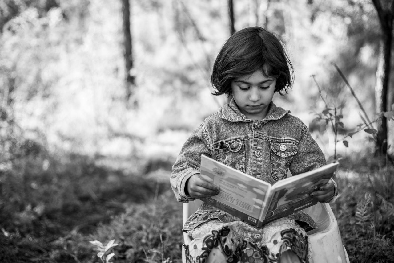 services-01 Black and white photo of a young girl reading outside in nature.